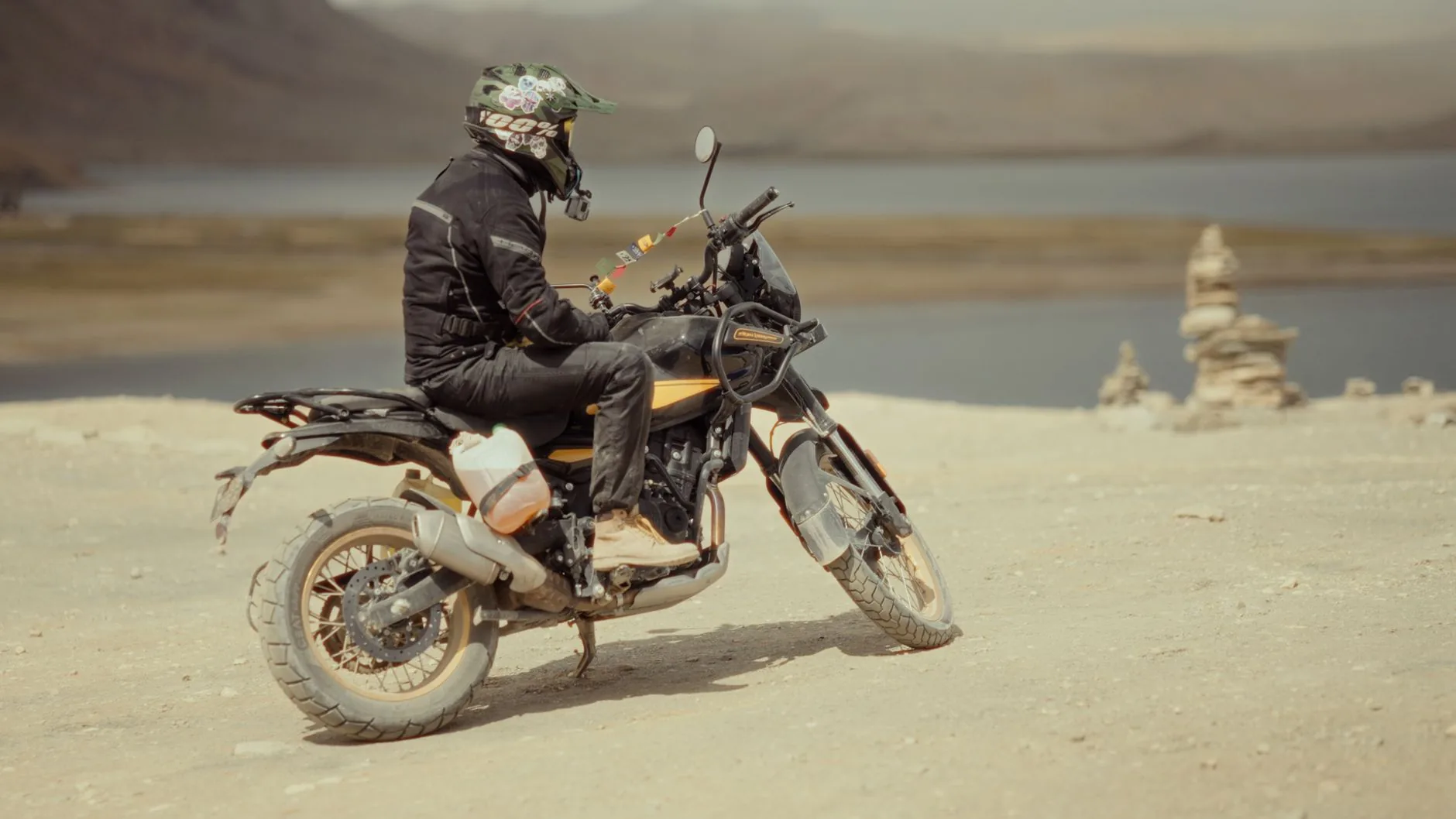 A woman in dusty gear stands beside her motorcycle with a winch.